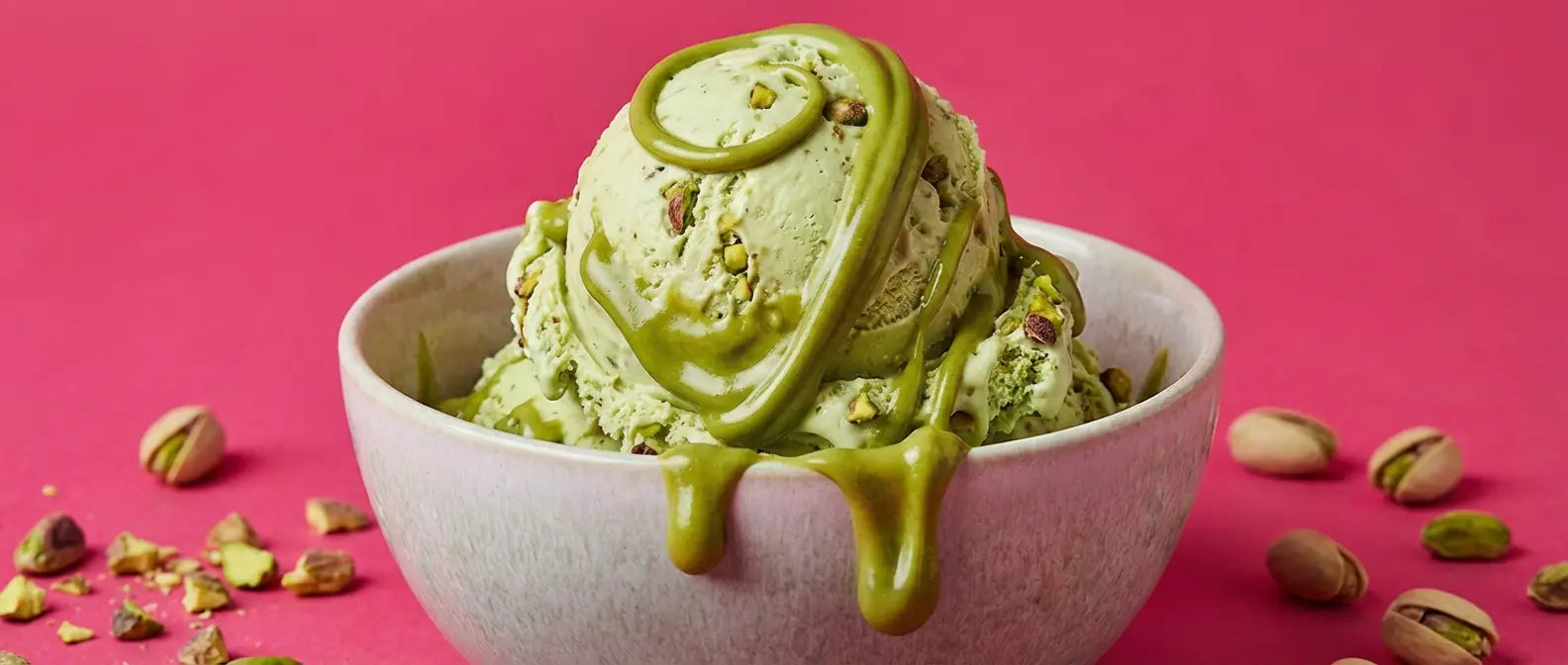 Pistachio ice cream scoops drizzled with Pistabella pistachio spread on a bright pink background.