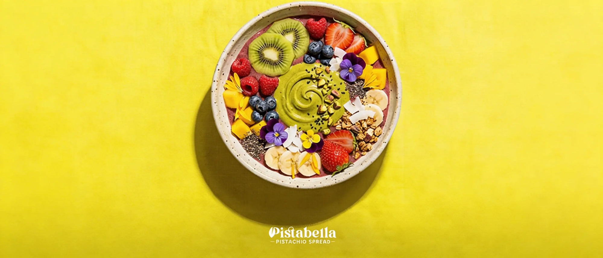 Smoothie bowl topped with a swirl of Pistabella pistachio spread, kiwi, berries, mango, and edible flowers.